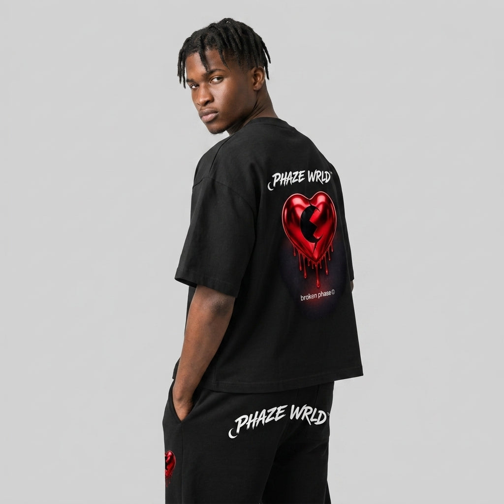 Back view of a premium black oversized streetwear t-shirt featuring a 3D metallic red dripping heart graphic and white "PHAZE WRLD" branding.