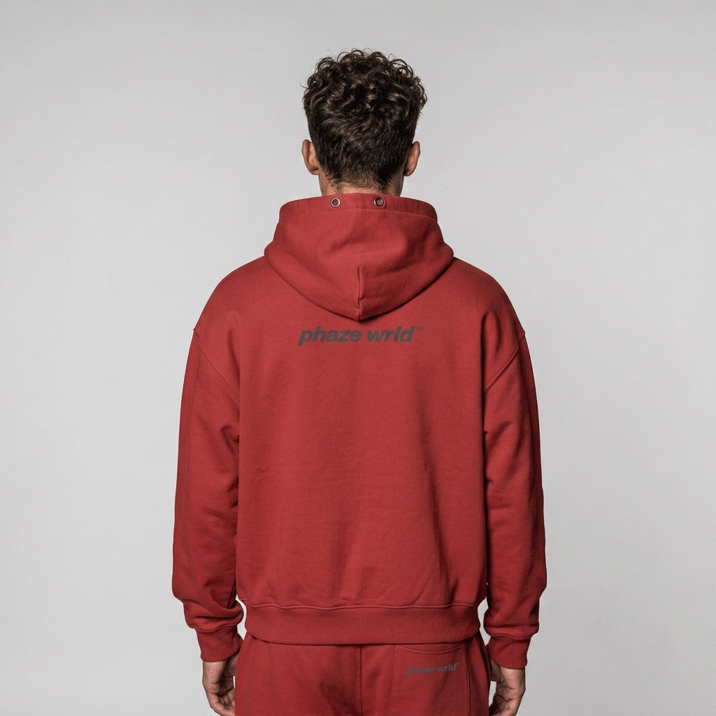 Back view of a premium brick-red oversized streetwear hoodie featuring a dark grey "phaze wrld" logo on the upper back.