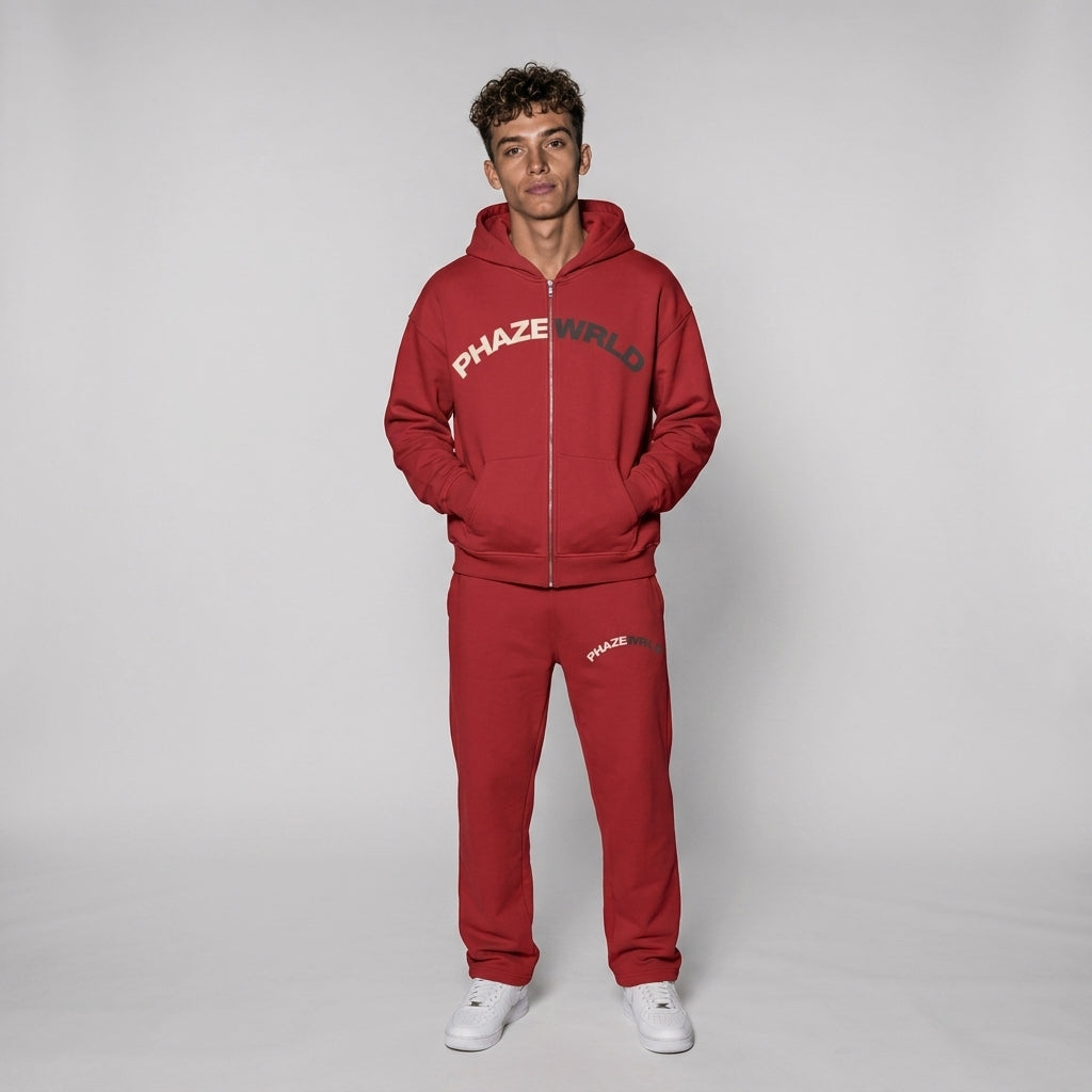 A premium crimson red zip-up streetwear hoodie with an arched two-tone Phaze Wrld chest graphic, drop-shoulder fit, and split kangaroo pockets.