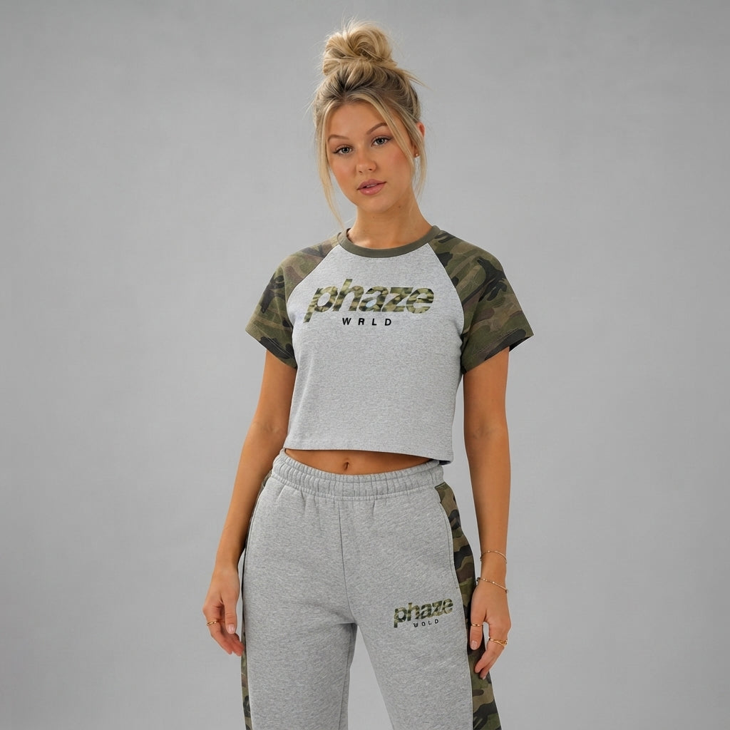A cropped heather grey raglan baby tee featuring green woodland camo sleeves and a central 'phaze wrld' camo wordmark graphic.