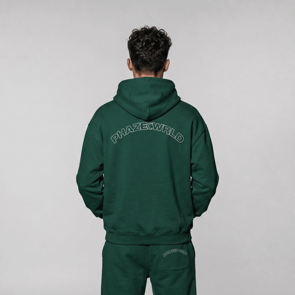 Back view of a premium forest green oversized streetwear hoodie featuring an arched white outline PHAZEWRLD wordmark on the upper back.