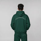 Back view of a premium forest green oversized streetwear hoodie featuring an arched white outline PHAZEWRLD wordmark on the upper back.