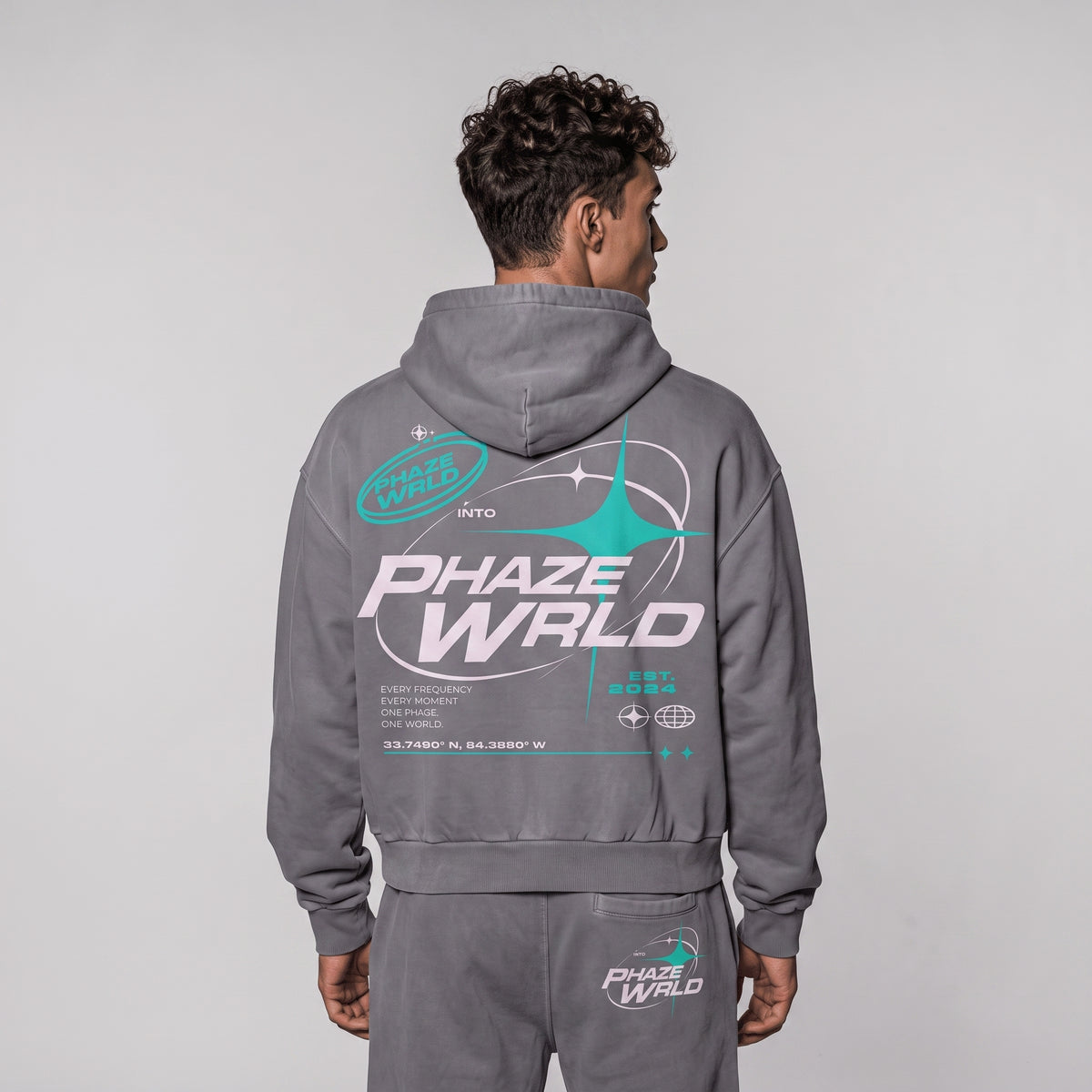 Close-up back view of a model in the grey Into The Phaze Boxy Hoodie, focusing on the large white and teal futuristic print.