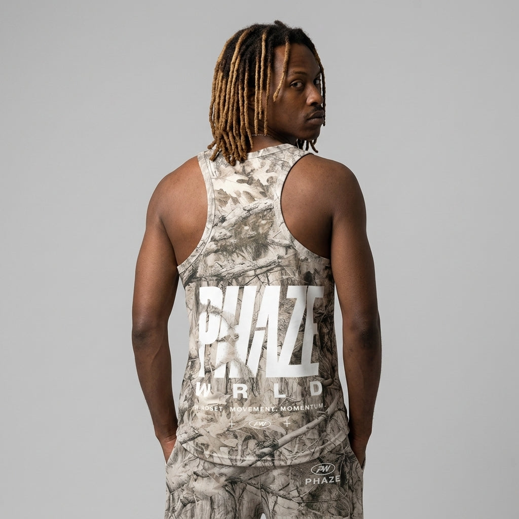 A streetwear sleeveless tank top featuring a beige and taupe real-tree camouflage pattern and a bold white PHAZE WRLD chest logo graphic.