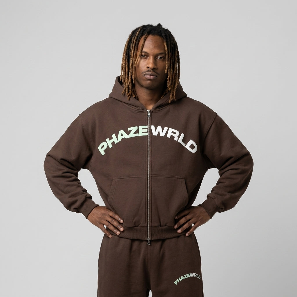 A studio lookbook photo of a premium chocolate brown oversized zip-up streetwear hoodie with a mint green arched chest logo.