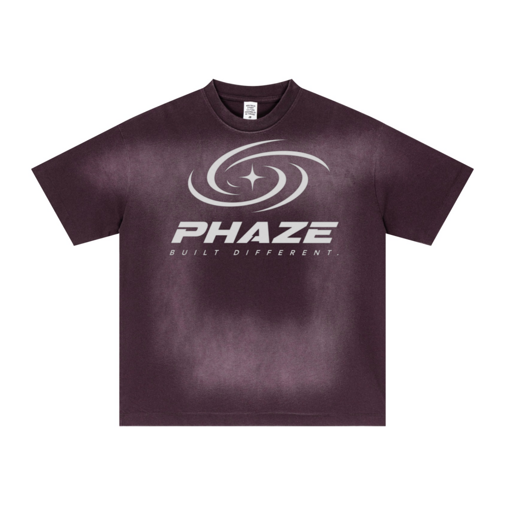 Purple streetwear oversized t-shirt featuring a futuristic silver PHAZE swirl graphic and "Built Different" text. Heavyweight cotton boxy fit.