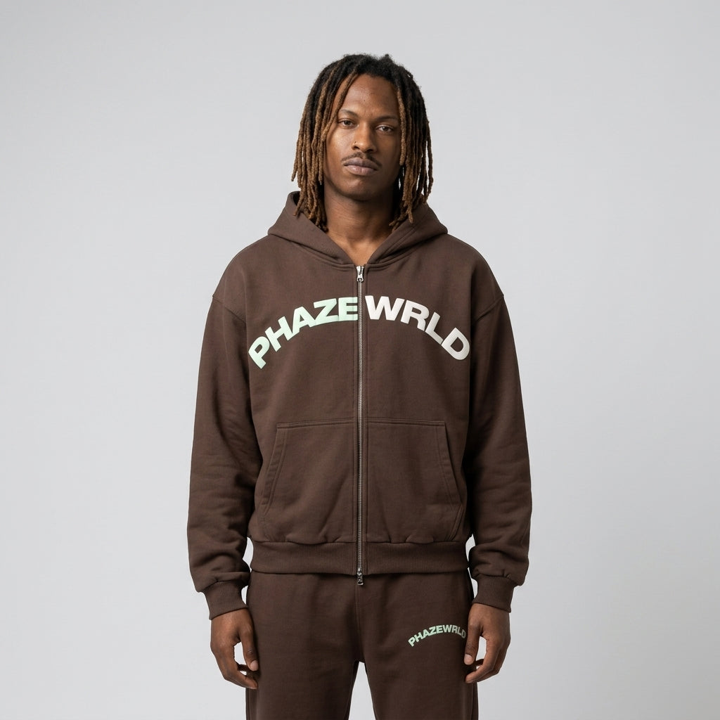 A studio lookbook photo of a premium chocolate brown oversized zip-up streetwear hoodie with a mint green arched chest logo.