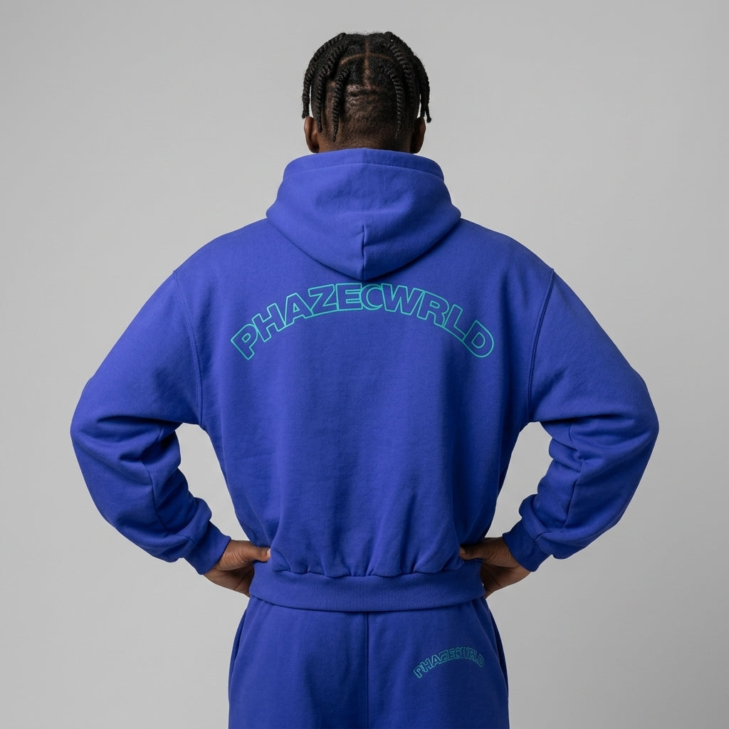 Back view of a premium royal blue oversized streetwear hoodie featuring a teal arched PHAZECWRLD outline graphic on the back.