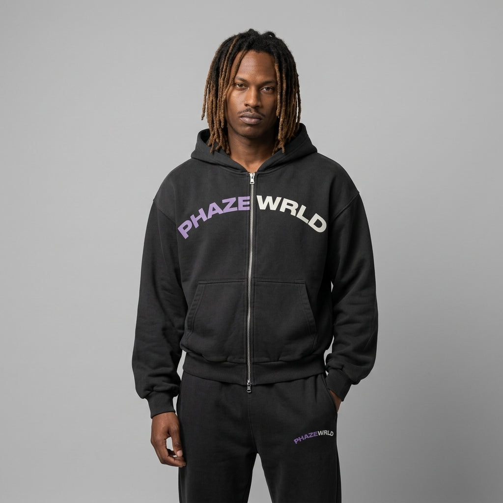 A premium washed black oversized streetwear zip-up hoodie featuring a purple and white arched PHAZEWRLD logo graphic on the chest.